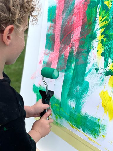 kleiner Junge erstellt ein abtraktes Bild mit einer Farbrolle